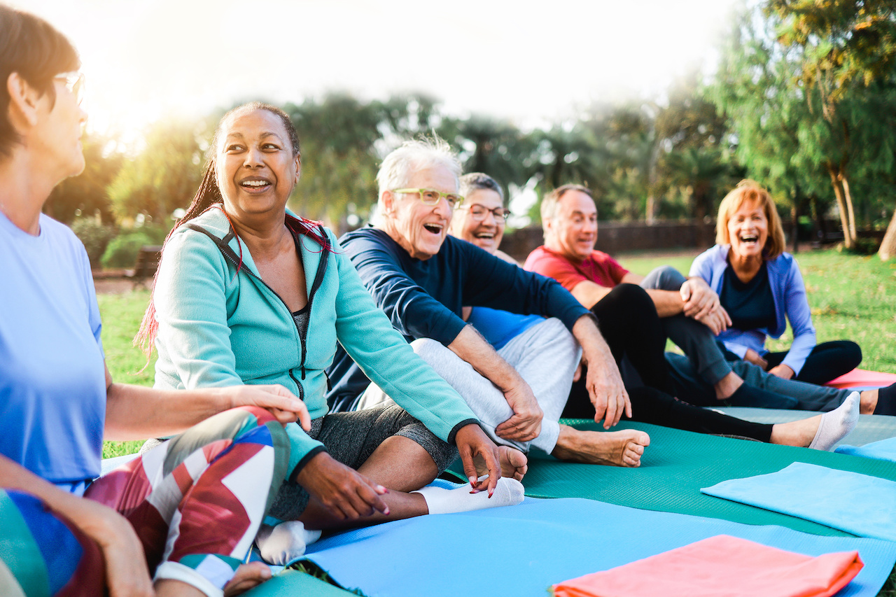 Happy senior people after yoga sport class having fun sitting outdoors in park city